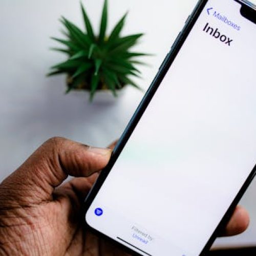 A close-up view of a smartphone screen displaying the email inbox, held by an adult's hand.